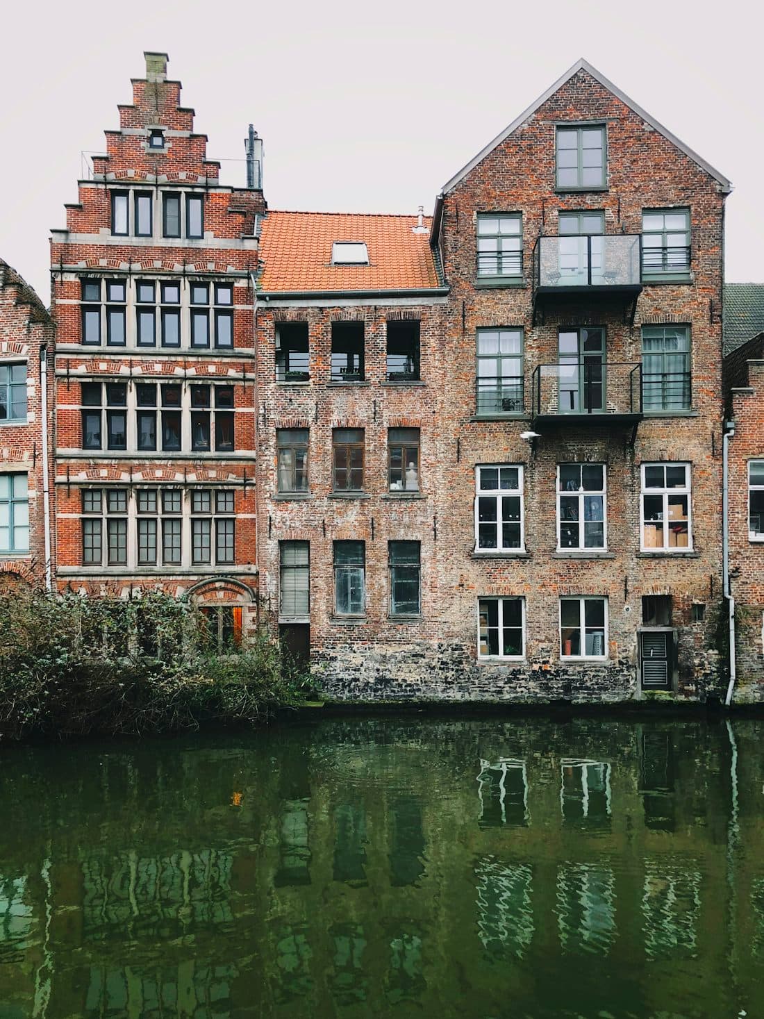 Brick canal houses in Ghent with a stepped gable, reflected in still water